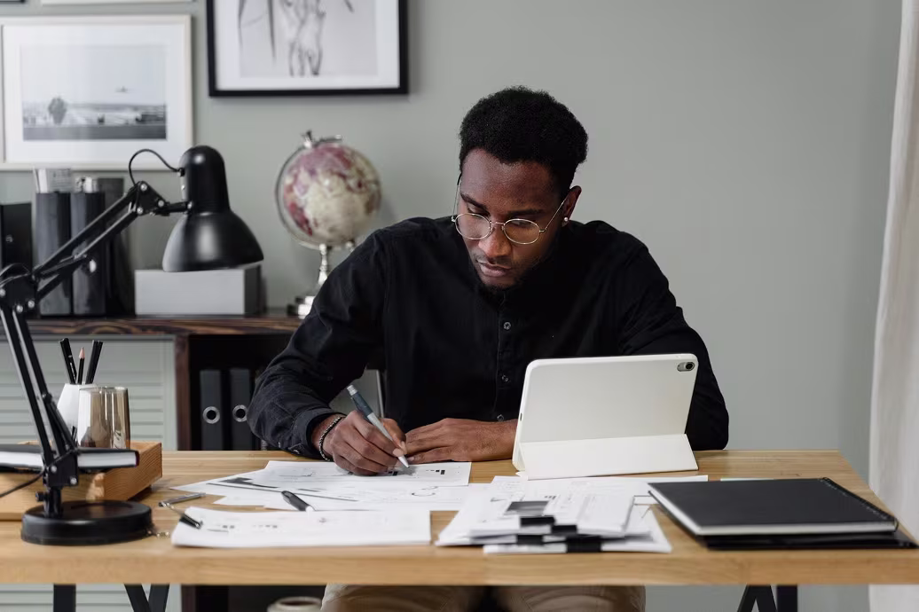 men working on his desk while writing on a paper